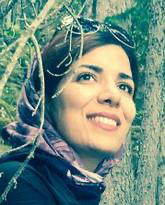 Close-up portrait of a young female who appears to be Asian, wearing a full smile and a scarf partially over her head, with sunglasses resting on top of her head. The background has trees.